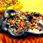 A close up photo of a cupcake with dark blue icing and multicoloured sprinkles.