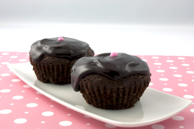 Deep Chocolate Brownie Cupcake A close up photo of 2 chocolate brownie cupcakes with a pink ball on a pink polka dot paper.