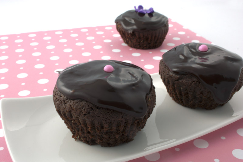 Deep Chocolate Brownie Cupcake A photo of 3 chocolate cupcakes, decorated with 2 pink balls, and one with a purple flower on top of a pink polka dotted paper.