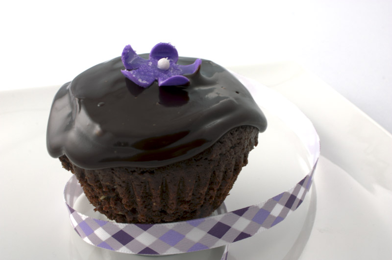 Deep Chocolate Brownie Cupcake A close up photo of a chocolate brownie cupcake with a purple flower and a purple ribbon.
