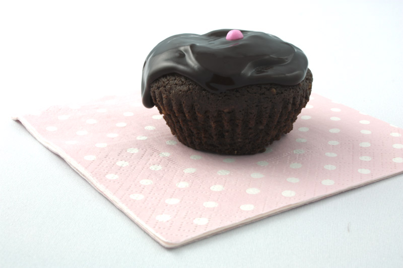 Deep Chocolate Brownie Cupcake A close up photo of a chocolate brownie cupcake with a pink ball on a pink napkin.