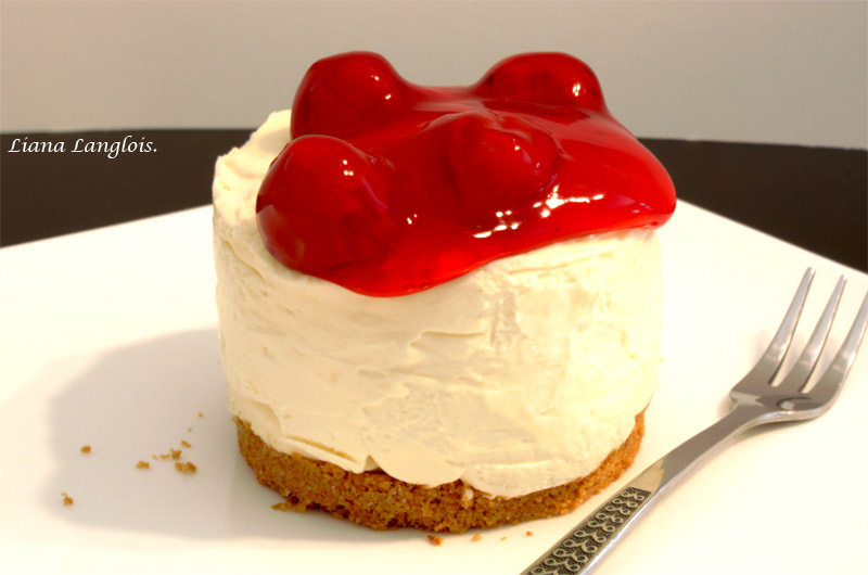 Cheesecake A close up photo of a cheesecake dessert with cherry topping on a white plate as well as a small silver fork on the side.