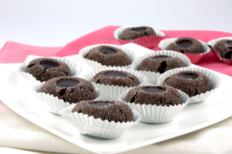 A close up photo of chocolate thumbprints on a white plate with a pink napkin.