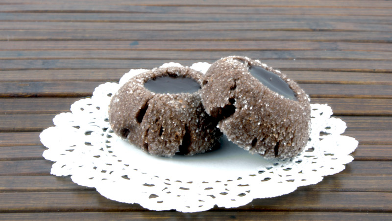A close up photo of 2 chocolate thumbprints on a white doilie placed on a wooden placemat.