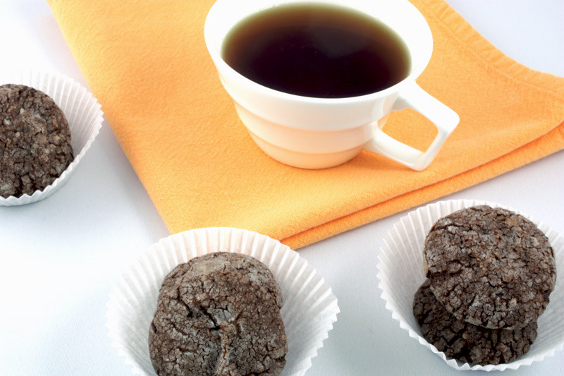 A photo of dark chocolate-almond crackles in 3 white paper cups with a white cup of tea on an orange napkin.
