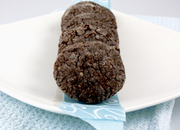 A close up photo of dark chocolate-almond crackles on a blue ribbon on a white dish placed on a blue tea towel.
