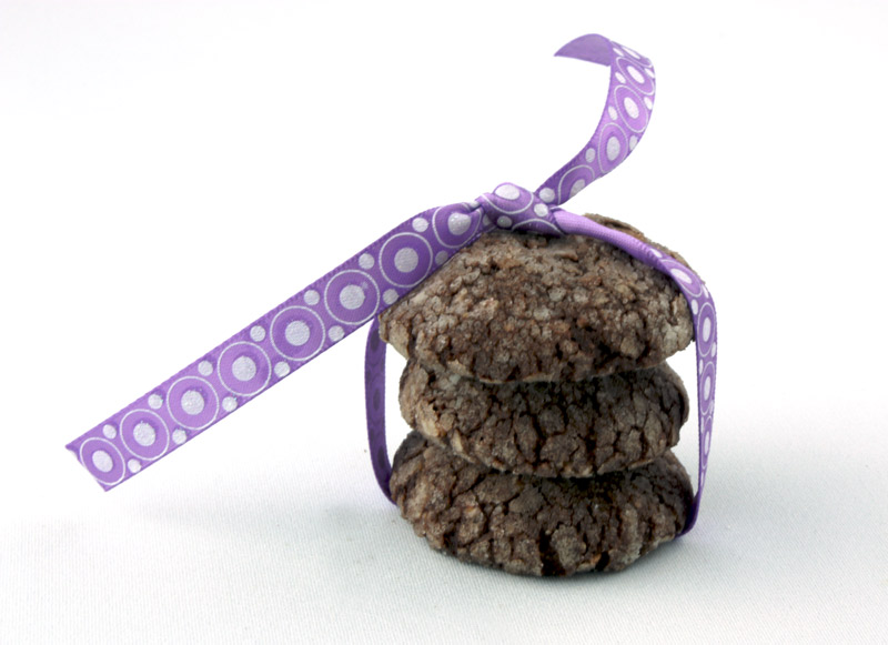 A close up photo of 3 dark chocolate-almond crackles tied in a purple ribbon.