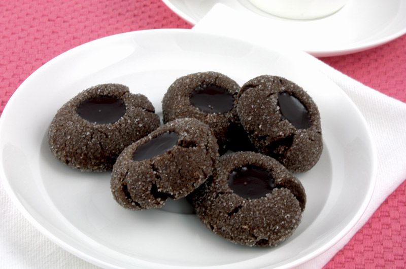A close up photo of chocolate thumbprints on a white dish on a pink napkin with a white cup and saucer.