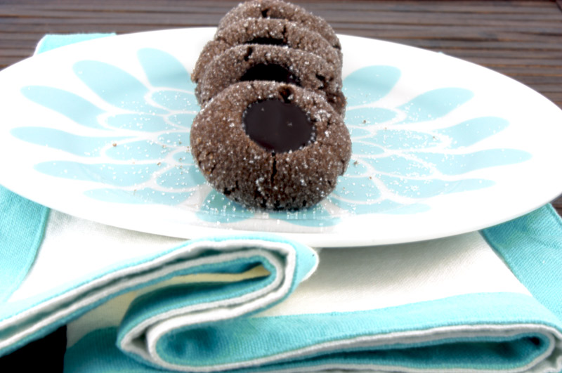 A photo of chocolate thumbprints on a blue flowered white plate on a blue and white napkin placed on a wooden placemat.