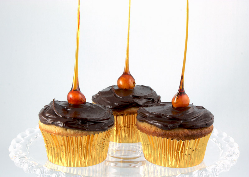 Candied-Hazelnut Cupcakes A close up photo of 3 candied-hazelnut cupcakes on a glass cake stand.