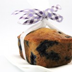 A close up photo of a blueberry banana walnut loaf wrapped in a purple ribbon and parchment paper.
