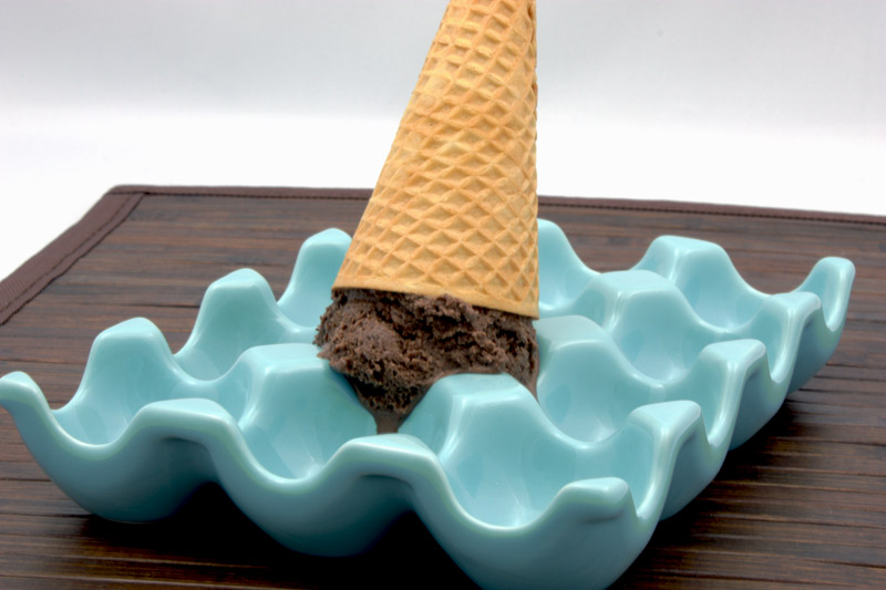 Ben & Jerry's Chocolate Ice Cream A photo of an upside down sugar cone with chocolate ice cream in a blue egg tray on a wooden placemat.