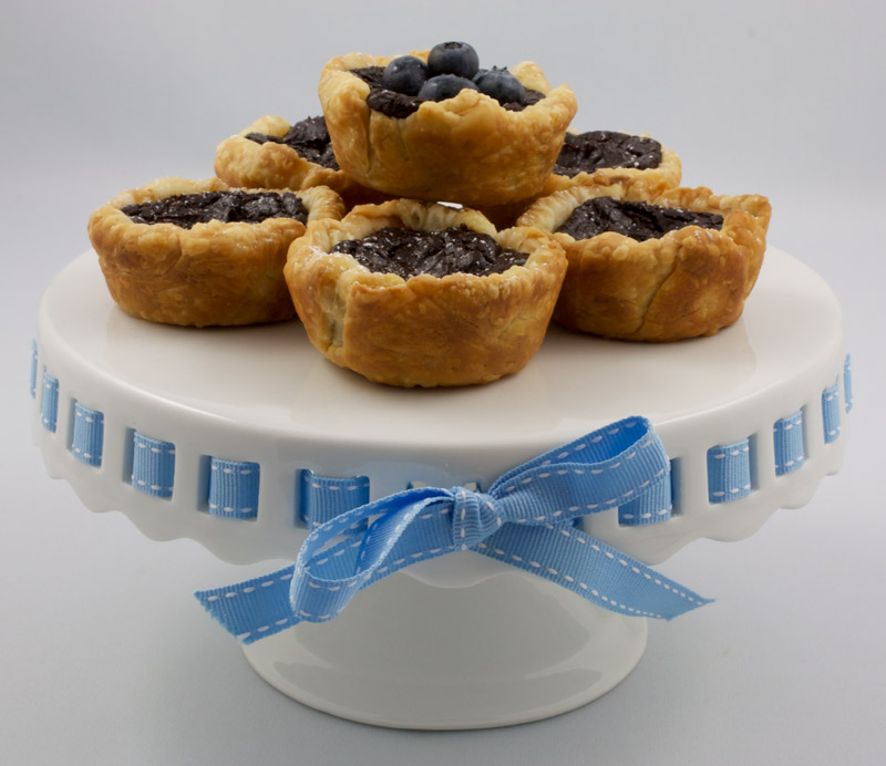 Chocolate Custard Tartlettes A photo of chocolate custard tartlettes on a white cake stand with a blue ribbon.