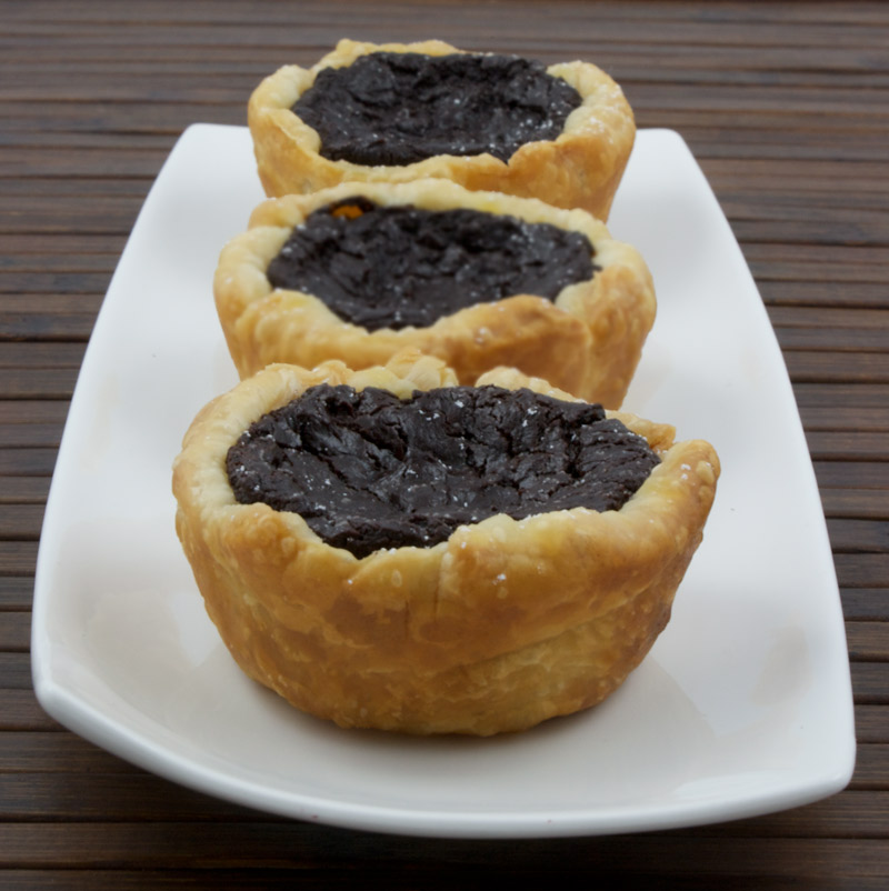 Chocolate Custard Tartlettes A photo of 3 chocolate custard placed on a white plate on a wooden placemat.