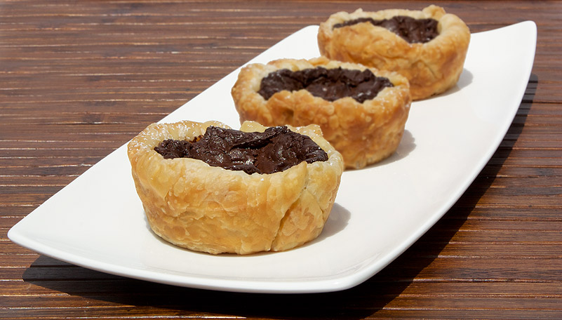 Chocolate Custard Tartlettes A photo of 3 chocolate custard tartlettes on a white dish placed on a wooden placemat.