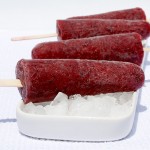 A photo of 4 blueberry-banana fruit pops on a white dish with ice.