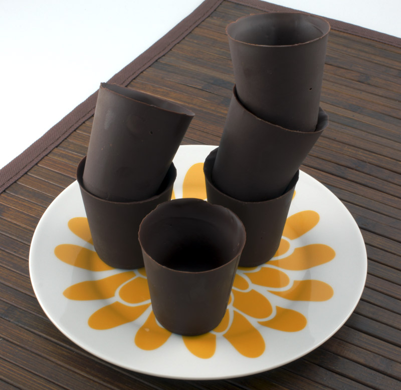 Edible Chocolate Cups A photo of stacked edible chocolate cups on a white plate on a wooden placemat.