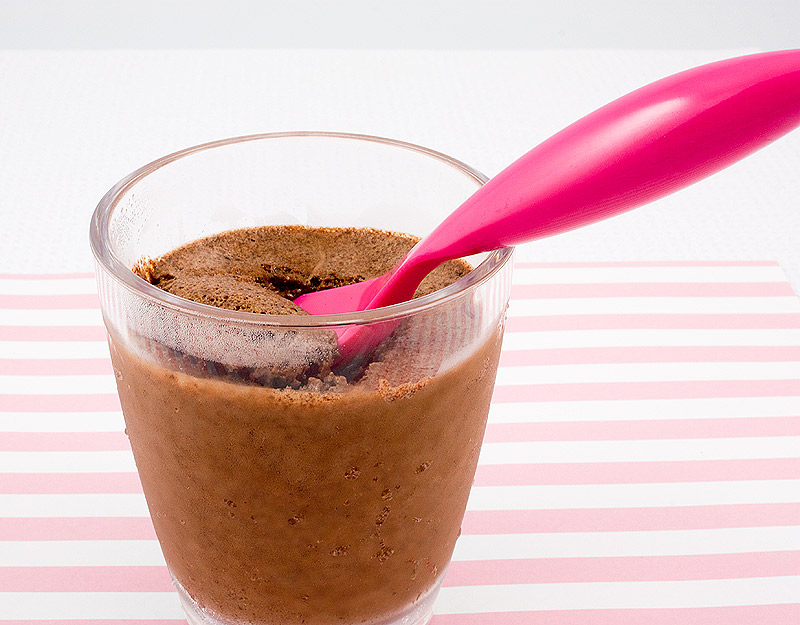 A close up photo of a double chocolate brownie semifreddo dessert with a pink spoon sitting on cup placed on a pink candy striped piece of paper.