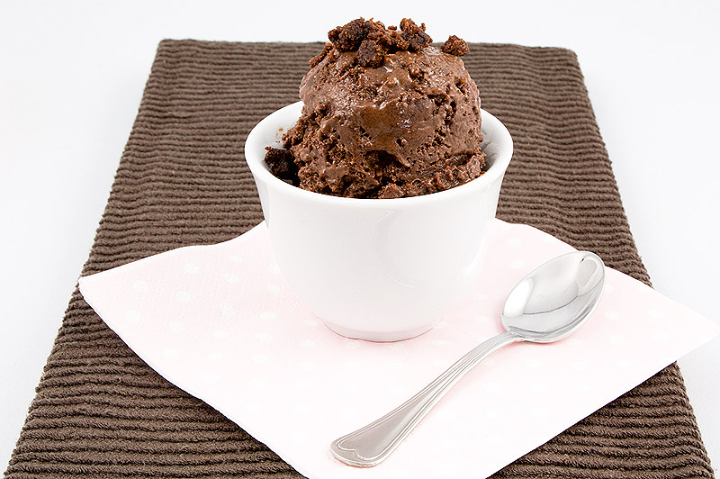 A photo of a double chocolate brownie semifreddo dessert garnished with brownie bits, sitting atop a pink polka dotted napkin with a spoon on a brown tea towel.