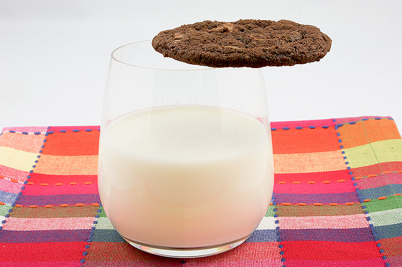 double-chocolate chunk cookies recipe, recipe for double chocolate chunk cookies, Martha Stewart cookie recipes, recipe for Martha Stewart's double chocolate chunk cookies A photo of a glass of milk with a double-chocolate chunk cookie sitting on the rim of the glass placed on a multi-coloured placemat.