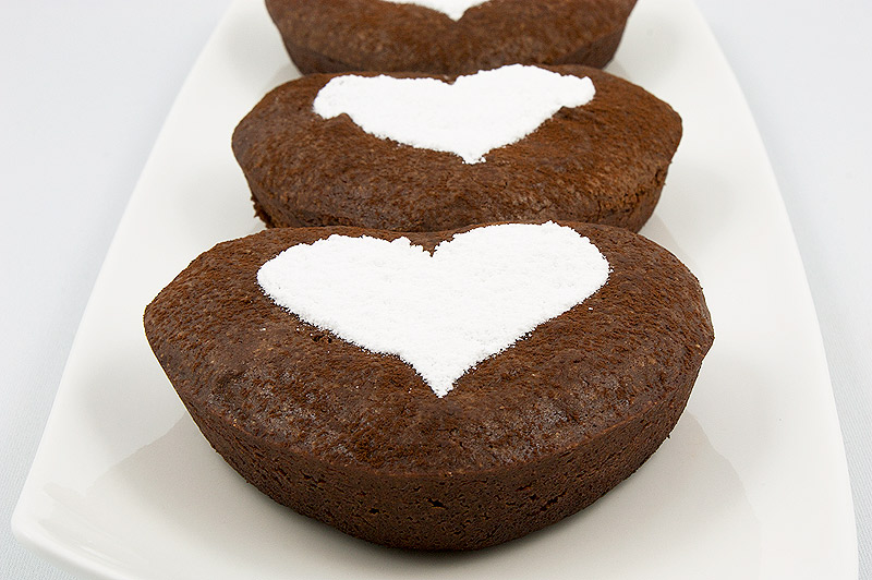 brownie truffles, brownie pops on a stick, Martha Stewart recipes, mini brownies A close up photo of 3 chocolate brownie hearts decorated with confectioners' sugar arranged in a row on a white dish.