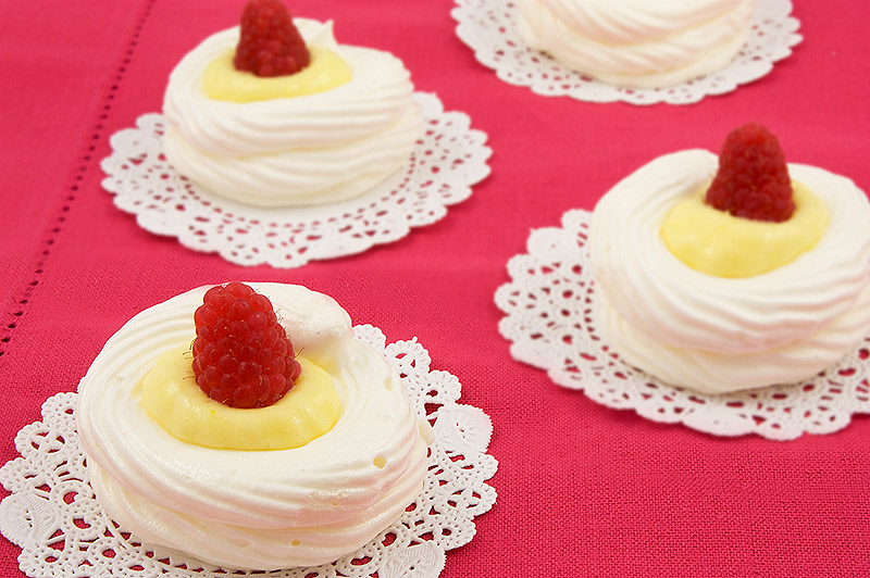 lemon curd meringue nests, meringue nests, meringue cups, easy lemon curd A photo of lemon curd meringue nests with raspberries on white doilies, placed on a pink placemat.