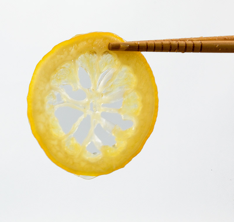 candied lemon slices, candied lemon peel, sugared lemon peel, garnish for meringue nests A photo of a candied lemon slice held with wooden chopsticks.