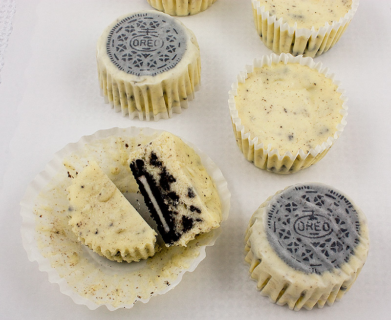 Oreo cookies and cream cheesecakes, Martha Stewart's cookies and cream cheesecakes recipe, easy recipe for Oreo cookies and cream cheesecake cupcakes A photo of 2 upside down Oreo cookies and cream cupcakes, 2 right side up and one cut in half on parchment paper.