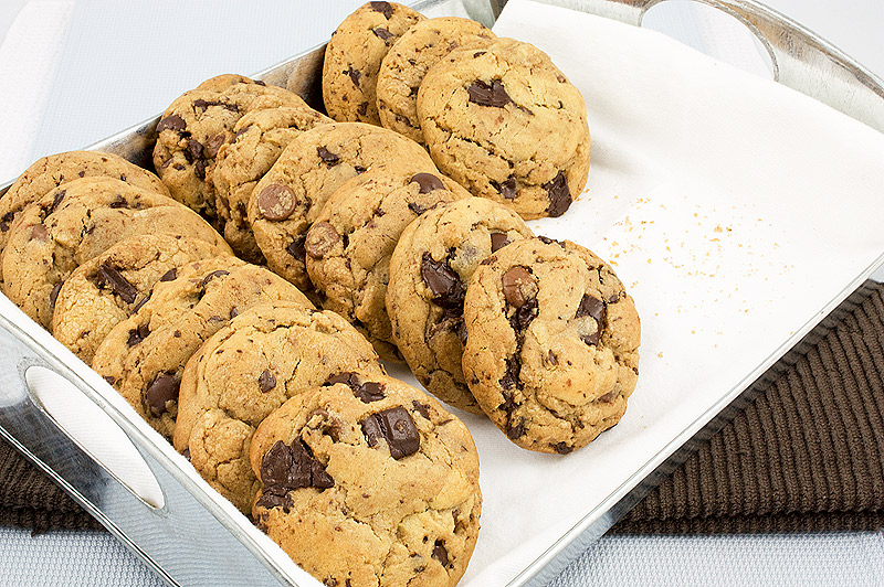 Jacques Torres's secret chocolate chip cookie recipe, Jacques Torres's recipe for chocolate chip cookies, bakery style chocolate chip cookies A photo of a tin tray with handles lined with a white cloth napkin contain rows of Jacques Torres's Secret Chocolate Chip Cookies placed on a brown tea towel.