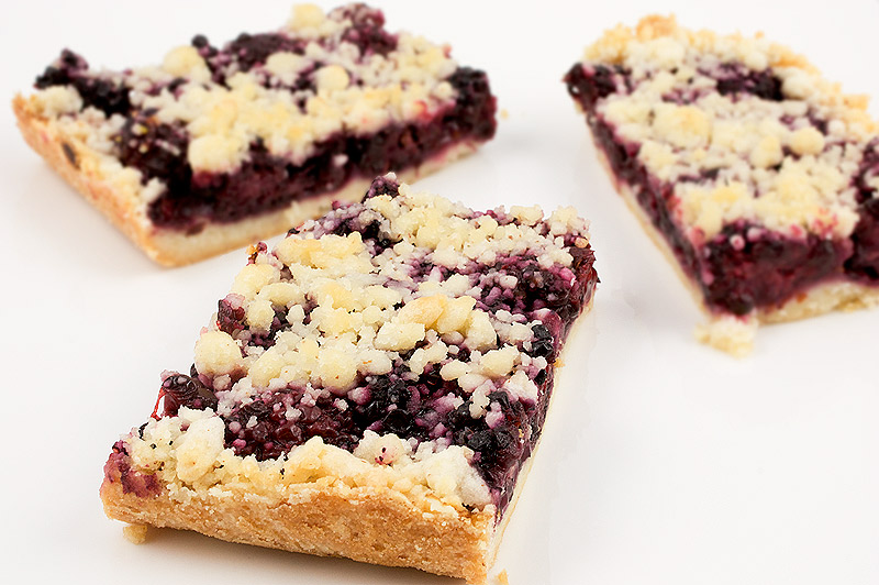 Martha Stewart's blackberry-almond shortbread squares recipe, recipe for Martha Stewart's blackberry crumble squares, Martha Stewart's recipe for almond shortbread A close up photo of 3 blackberry-almond shortbread crumb squares on a piece of parchment.
