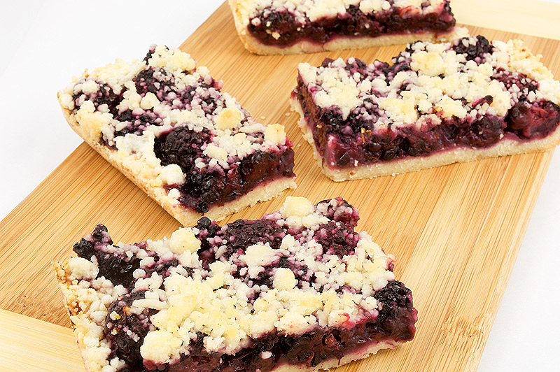 easy blackberry desserts, Martha Stewart's recipe for blackberry-almond shortbread crumble squares, Martha Stewart's berry crumb bar recipes A close up photo of 4 blackberry-almond shortbread squares on a wooden cutting board.