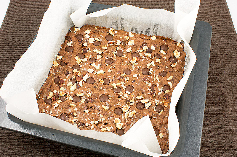 Robert's absolute best brownies recipe, Robert Steinberg's absolute best brownies recipe, easy chocolate dessert recipes A photo of a tin lined with parchment paper of just baked Robert's Absolute Best Brownies placed on a brown tea towel.