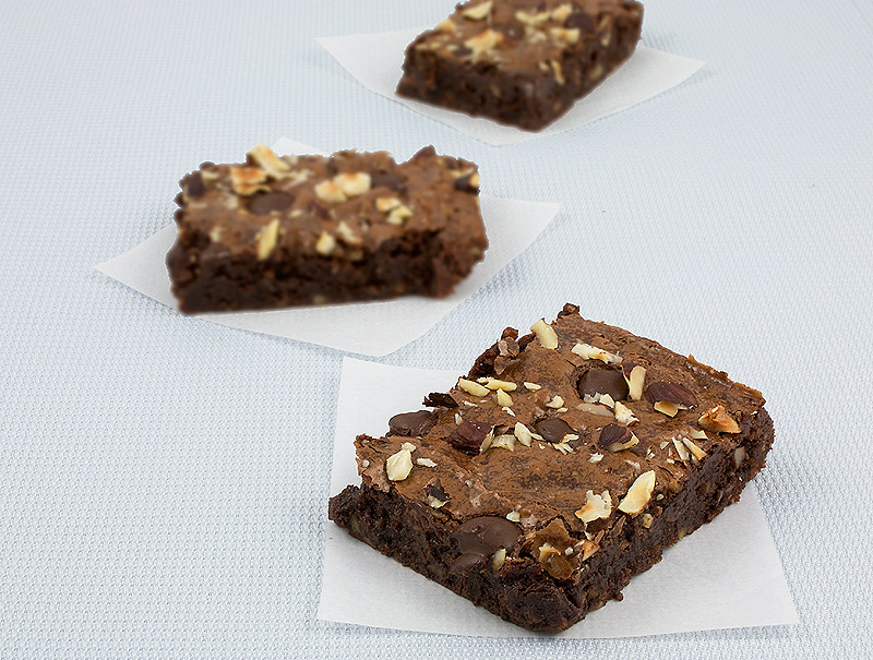 recipe for sinfully delicious brownies, decadent brownies recipe, David Lebovitz's brownie recipe A photo of 3 of Robert's Absolute Best Brownies placed on pieces of parchment paper on a light blue table runner.