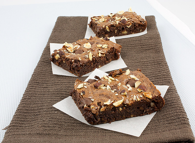 fudgy brownies recipe, recipe for David Lebovitz's brownies, brownies recipe from David Lebovitz's Ready for Dessert cookbook A photo of 3 of Robert's Absolute Best Brownies placed on small square pieces of parchment and placed on a brown tea towel.