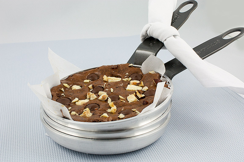 Robert Steinberg's absolute best brownies recipe, easy chocolate dessert recipes, easy brownie recipes A photo of a stack of 3 small skillets with the one on top lined with parchment and just baked Robert's Absolute Best Brownie dessert placed on a light blue table runner.