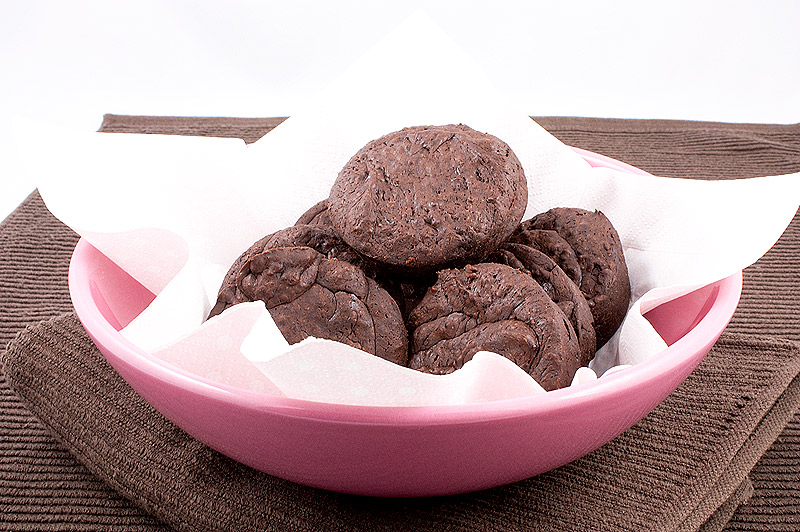 A photo of a pink bowl lined with a light pink paper napkin containing 8 flourless chocolate cakes placed on a brown tea towel.