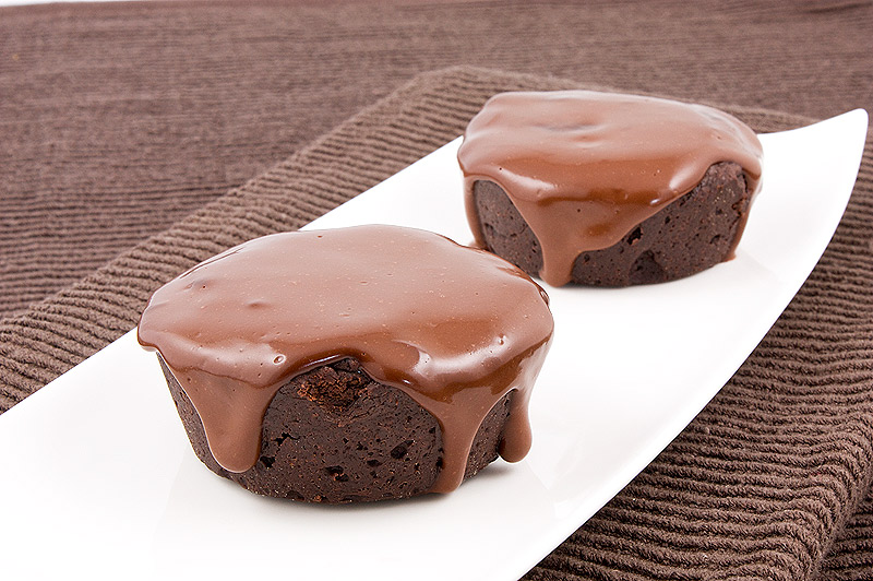 A photo of 2 flourless chocolate cakes with chocolate glaze on a white, rectangular plate placed on a chocolate brown tea towel.