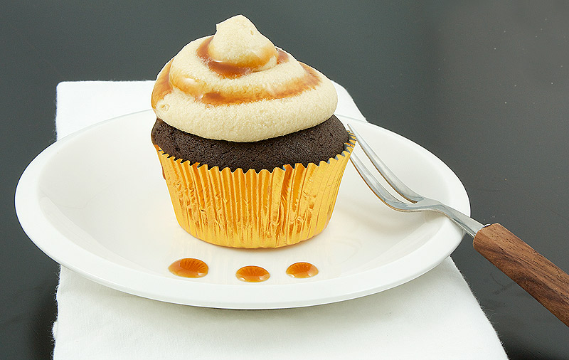 caramel buttercream frosting, quick and easy cupcakes, boozy cupcakes A up close photo of a Caramilk® Cream-Vodka Cooler Cupcakes with Caramel Buttercream Icing placed on a white dish with a dessert fork.