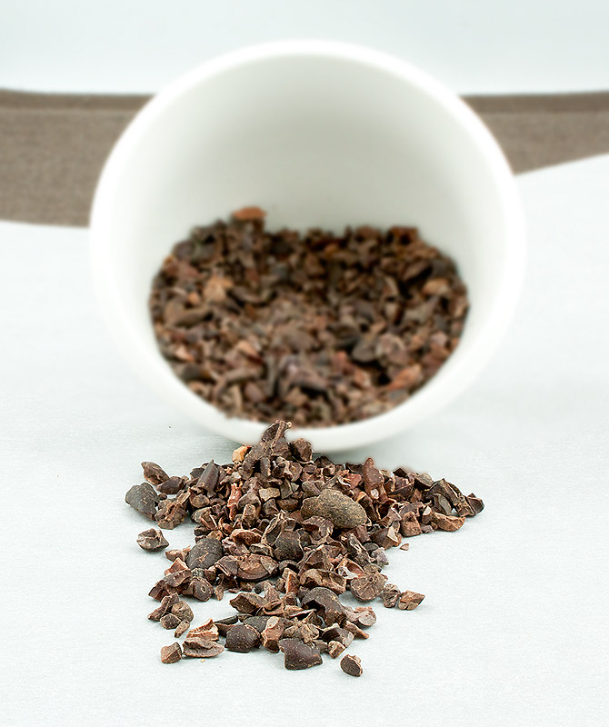 easy chocolate desserts, dessert photos, best dessert recipes A photo of a small, white bowl of cocoa nibs turned on its side and the cocoa nibs are tumbling out onto a piece of parchment paper.