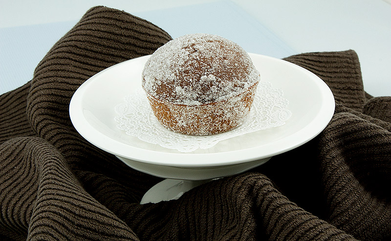 breakfast ideas, easy chocolate recipes, chocolate muffin recipes A photo of a sugared, chocolate-spiced muffin on a small white plate wrapped in a brown tea towel.