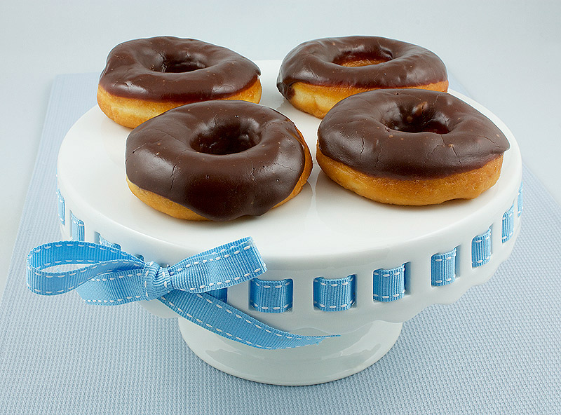 chocolate donut, chocolate glaze, making donuts, donut recipes A photo of 4 chocolate glazed donuts on a white cake plate with pale blue ribbon.