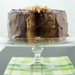 A photo of David Lebovitz's Banana Cake with Mocha Frosting and Salted Candied Peanuts with a slice removed and displayed on a glass cake stand.