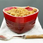 fruit crisp recipe, simple fruit dessert, crumble toppings A photo of a Pear, Rhubarb and Raspberry Fruit Crumble dessert in a red, heart-shaped ramekin placed on a white napkin with a dessert spoon.