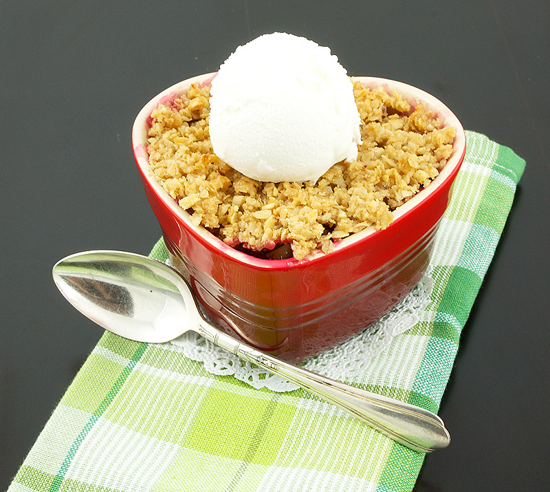 fruit crumble, quick and easy desserts, rhubarb crumble recipe A photo of a Pear, Rhubarb and Raspberry Fruit Crumble dessert topped with vanilla ice cream in a red, heart-shaped ramekin placed on a multi-coloured napkin with a dessert spoon.