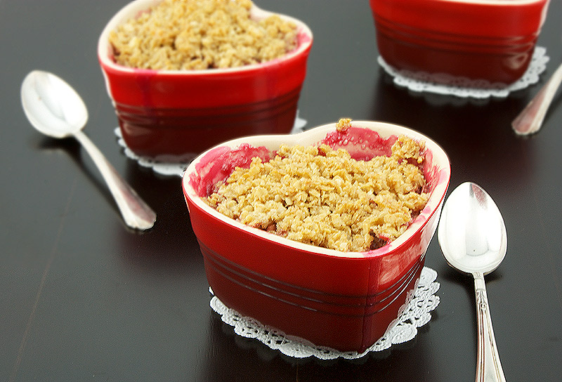 fruit crumble, quick and easy desserts, rhubarb crumble recipe A photo of 3 Pear, Rhubarb and Raspberry Fruit Crumbles desserts in red heart-shaped ramekins placed on white doilies and pictured with a dessert spoon.