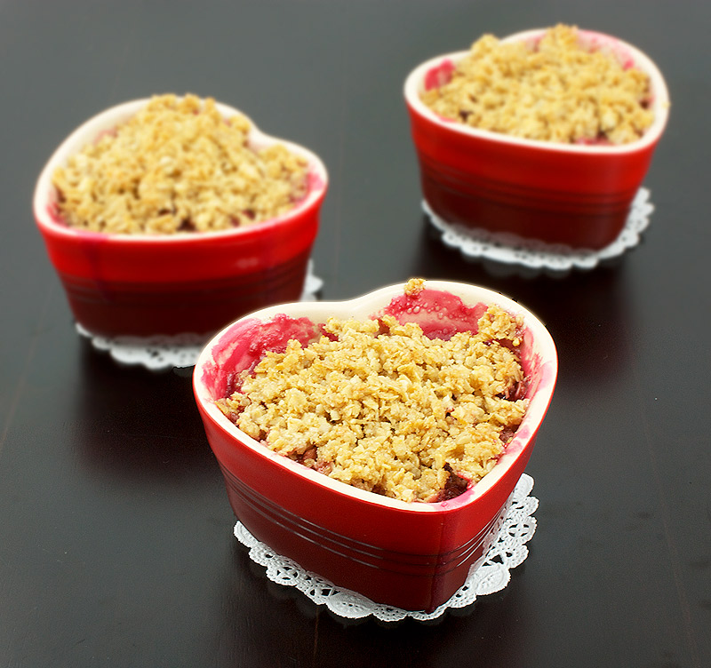 crumble toppings, toppings for fruit crumble, easy crumble topping A photo taken looking down onto 3 Pear, Rhubarb and Raspberry Fruit Crumble desserts in red, heart-shaped ramekin placed on white doilies.