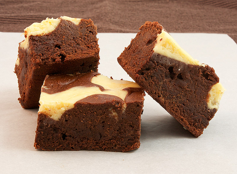 A photo of 3 Baileys® Cheesecake Swirl Chocolate Brownie squares on a piece of non-stick baking paper.