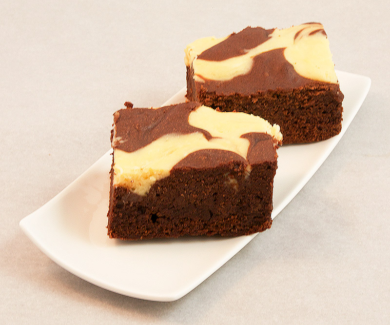 A photo of Donna Hay's Cheesecake Swirl Chocolate Brownies placed on a white, rectangular dessert plate.