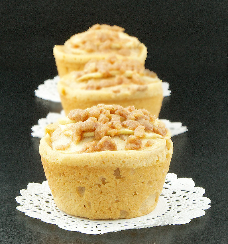 Warm Apple Cinnamon Crumb Cakes with Calvados A photo of three Warm Apple Cinnamon Crumb Cakes with Calvados on white doilies placed in a row.