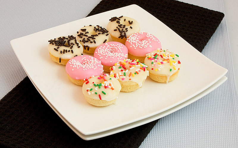 A photo of a plate of white chocolate baked doughnuts with vanilla glaze and decorated with various sprinkles.